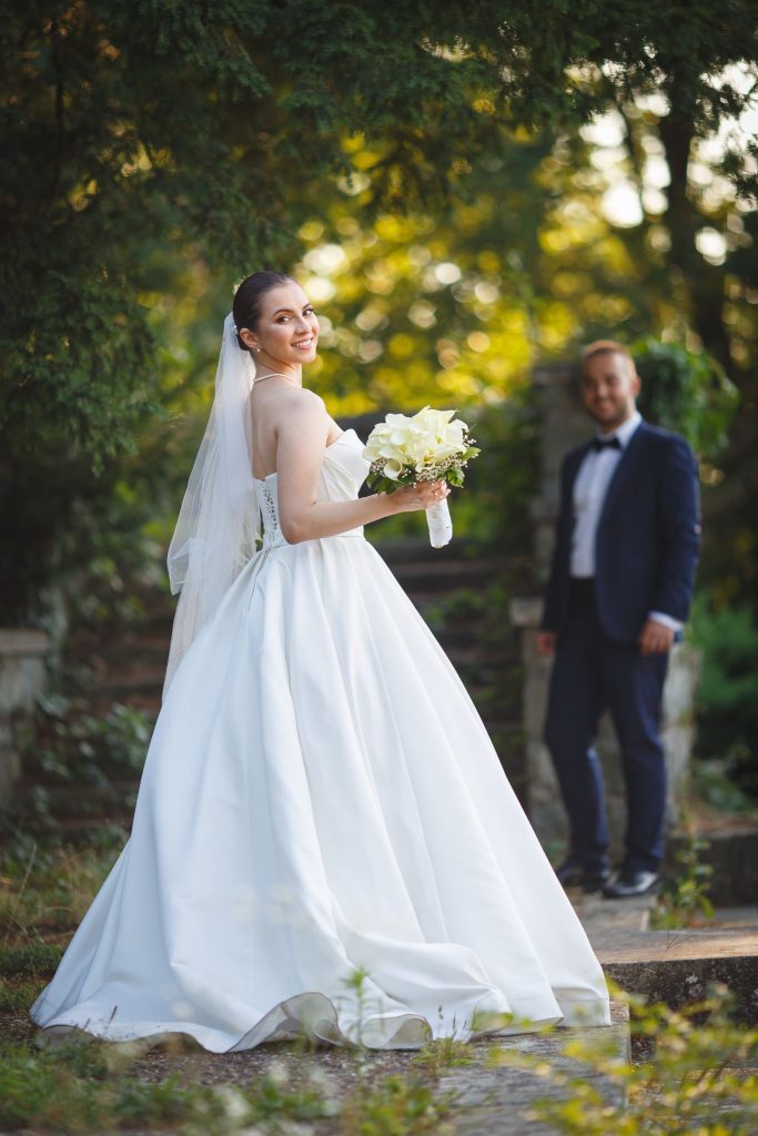 Bride holding a bouquet of white roses with groom blurred in the background