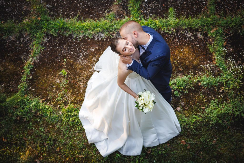Bride laughing while groom kisses her, both embracing from a distance