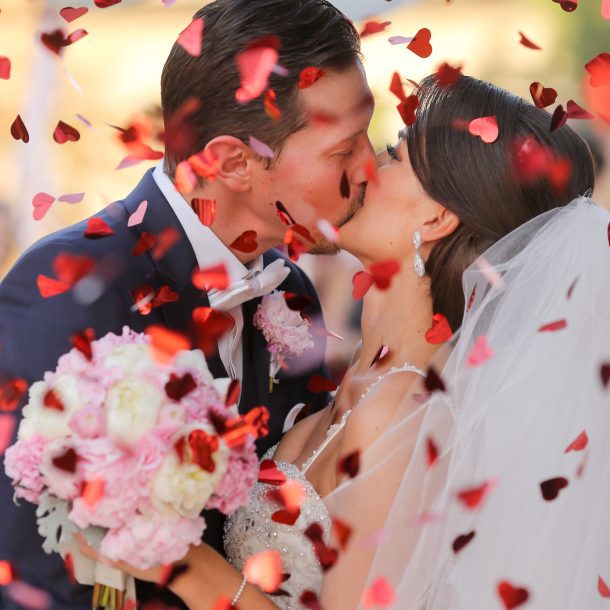 Bride and groom kissing as red rose petals fall around them