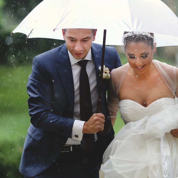 Close-up of bride and groom running in the rain under an umbrella, full of joy