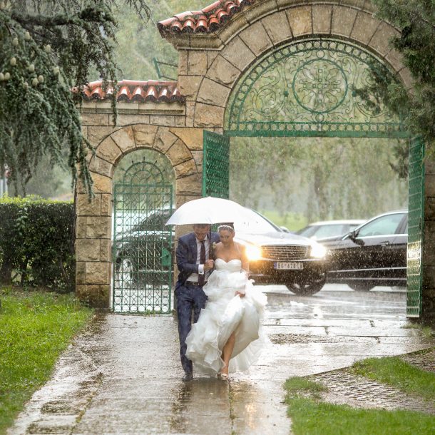 Bride and groom running joyfully in the rain under an umbrella