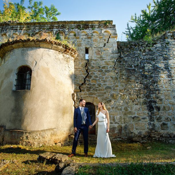 Bride and groom holding hands and gazing ahead near a historic tower